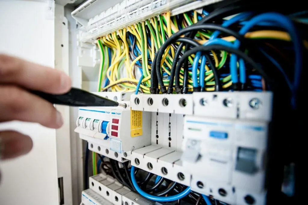 Electrician testing connections inside a circuit breaker panel with color-coded wiring.